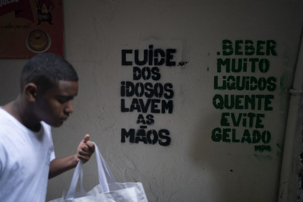 Um homem passa em frente a recados de conscientização sobre o coronavírus na Rocinha, Rio de Janeiro - Foto: Leo Correa / AP